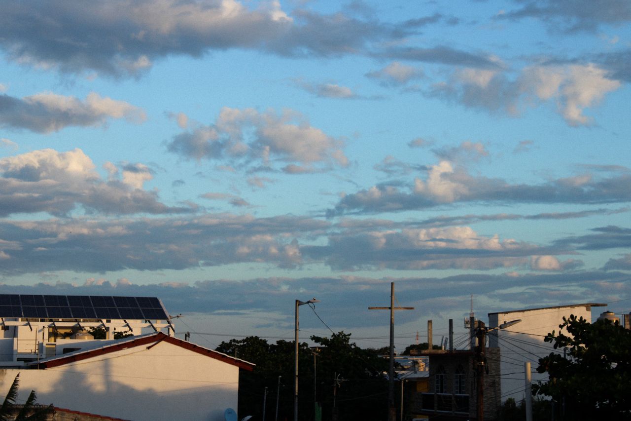 A scenic view of rooftops with solar panels under a cloudy blue sky during the day.
